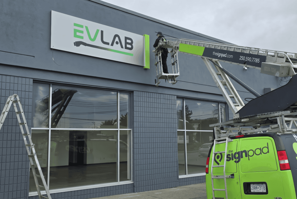 A technician installing the EV Lab sign on the building exterior.