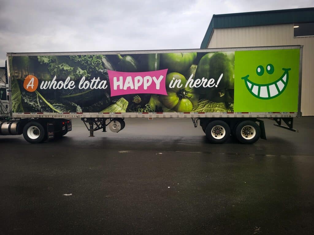 Large truck trailer with vibrant green vegetables and a smiling face graphic.
