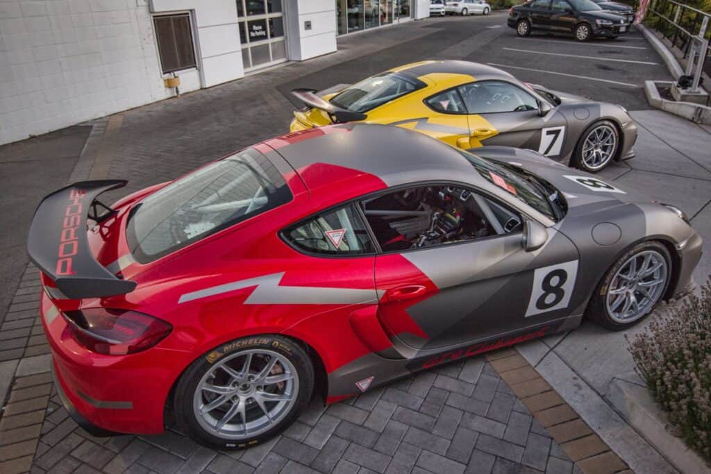 High-performance Porsche race cars featuring custom wraps parked outside a building.
