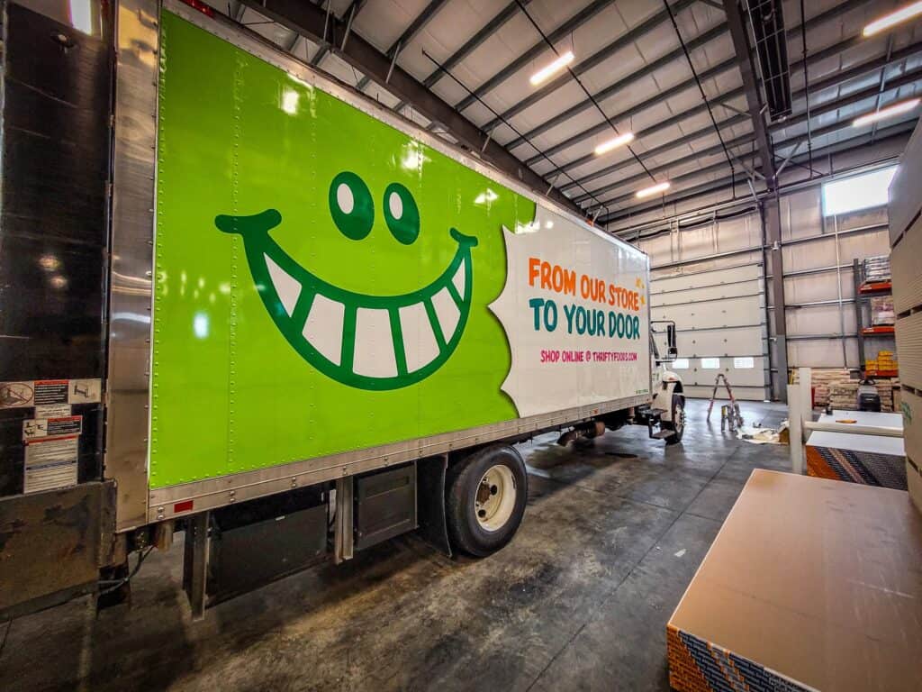 Delivery truck with a large, cheerful green smiley face sign.