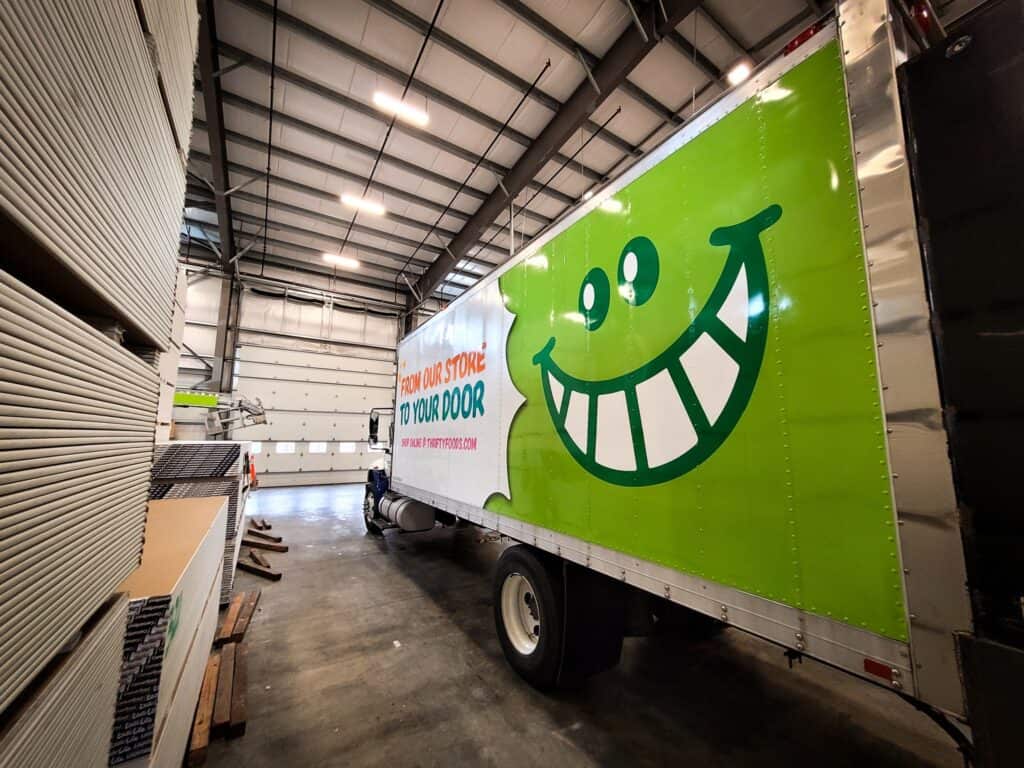 Signage truck with a bright green background and a large smiling cartoon face for custom signs and v.
