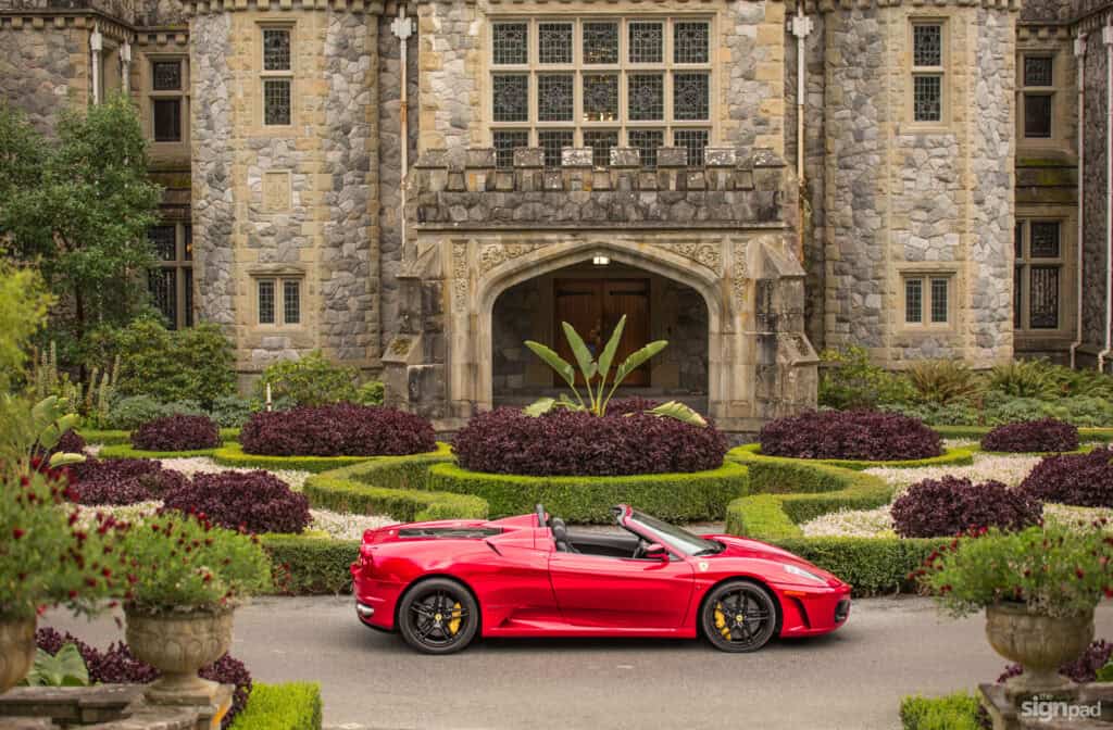 Luxury mansion with a red convertible sports car parked in front. Elegant stone architecture and lus.