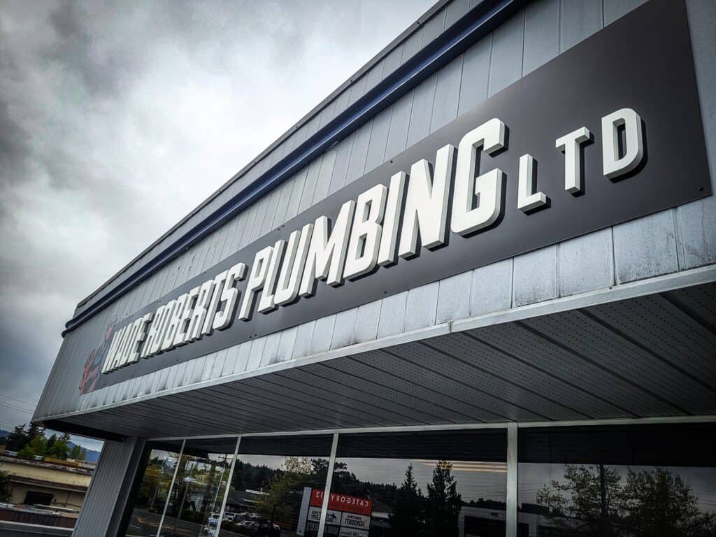 Exterior view of a custom business sign reading "LITTLE ROBERTS PLUMBING LTD" on a commercial buildi.