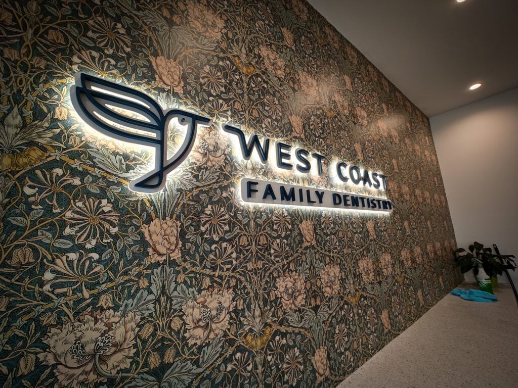 West Coast Family Dentist illuminated sign on floral wallpaper wall.