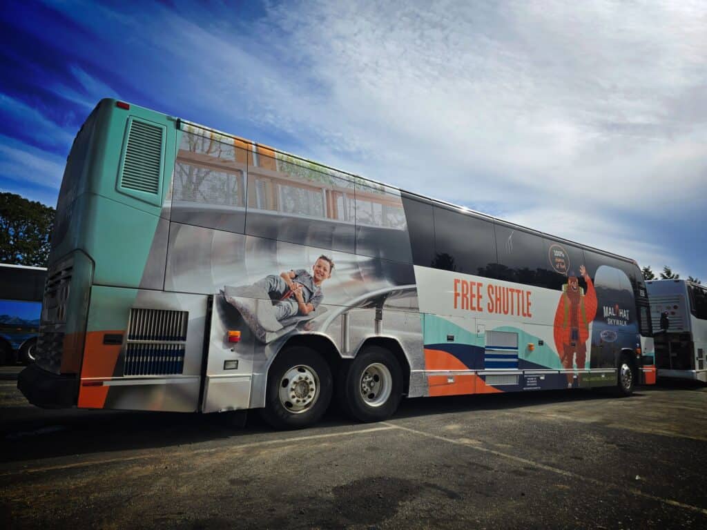 Bus wrap featuring a "Free Shuttle" sign and a passenger sitting on the side, promoting transportati.
