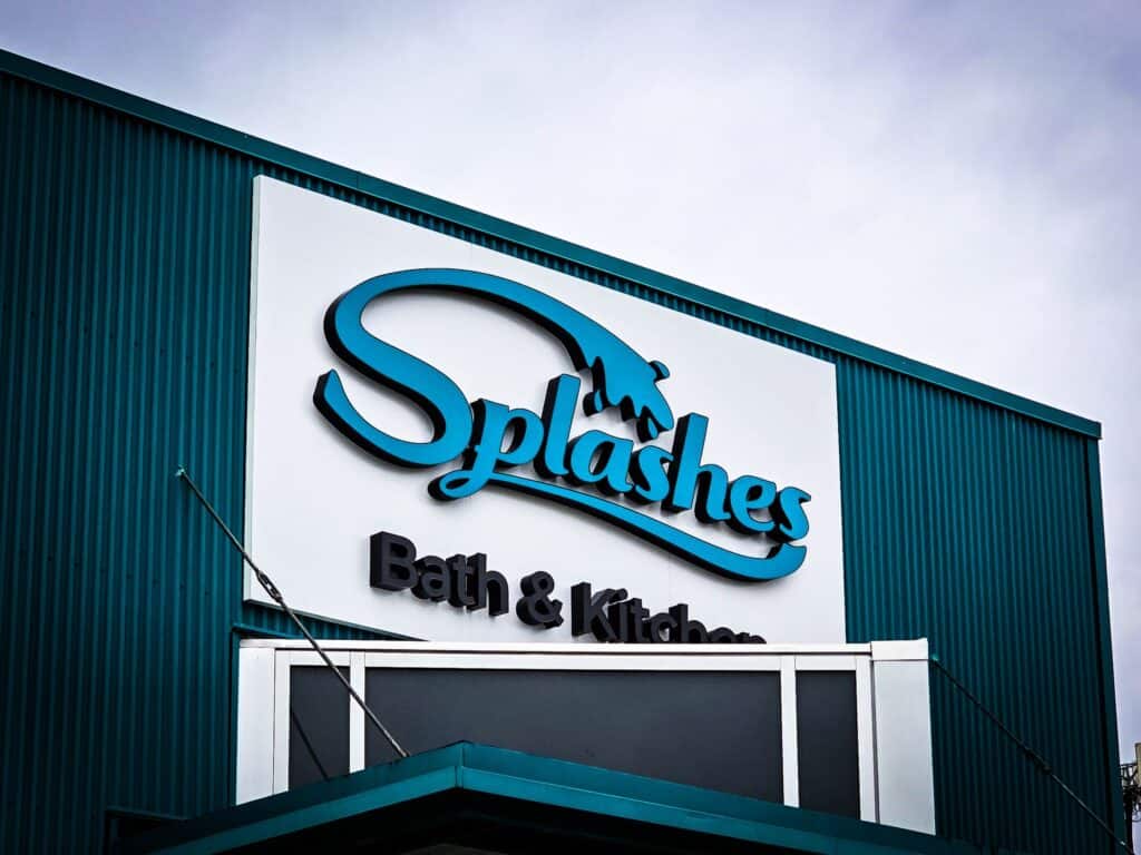 Exterior view of Splashes Bath & Kitchen store sign on a teal building facade.