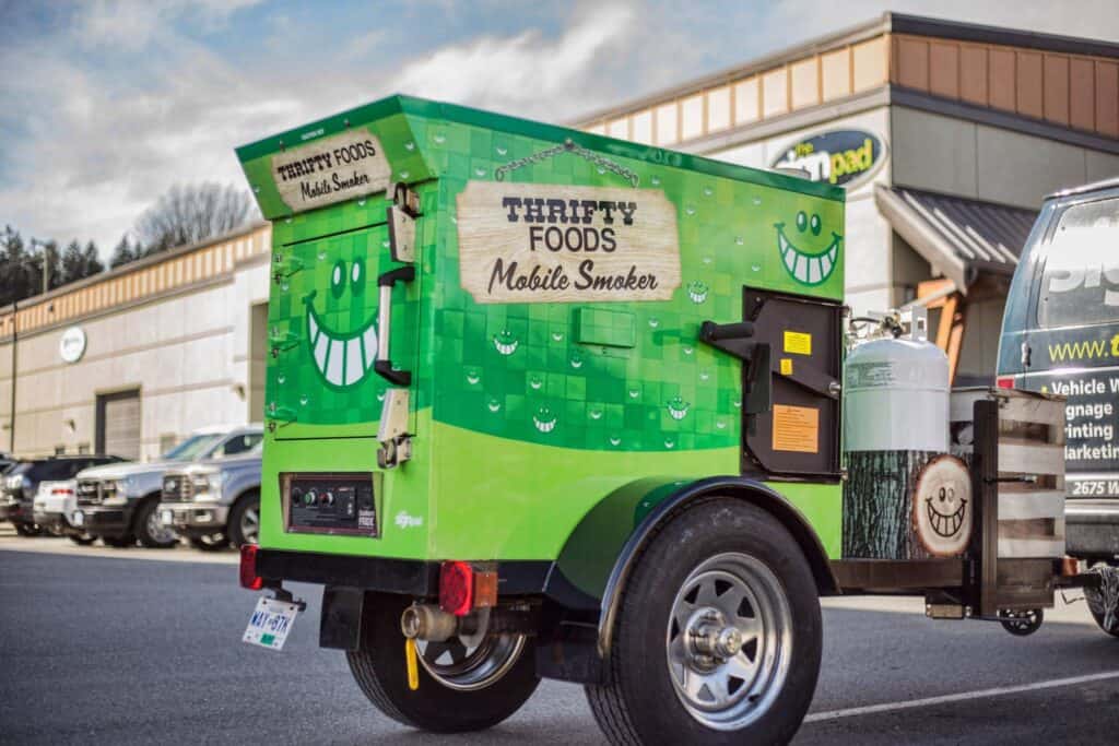 Mobile Smoker Food Truck with vibrant green wrap and smiling face design.