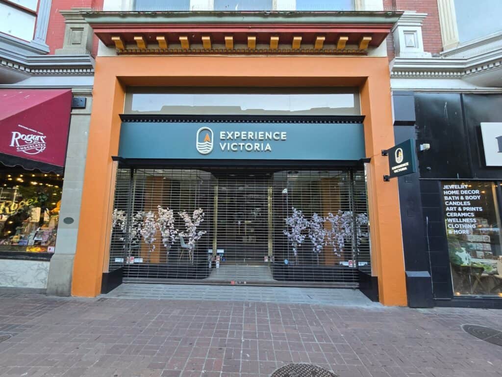Custom "Experience Victoria" sign on storefront with decorative trees behind glass.