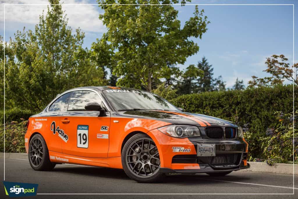 Race car with custom orange and black livery, number 19, on a city street.