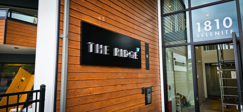 Black sign with white text reading "The Ridge" mounted on wooden exterior wall.