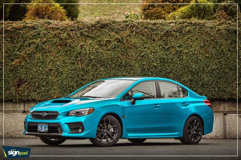 Subaru sedan in vibrant blue parked outdoors with a hedge background.