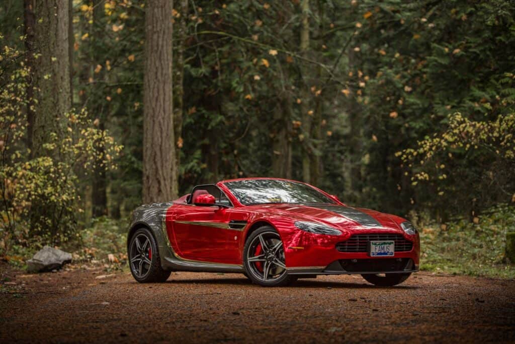 Luxury red sports car parked in a wooded area with tall trees and natural surroundings.