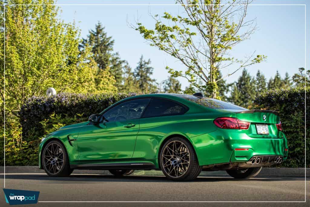 A sleek, green sports car parked on the street with a scenic background of trees and blue sky.