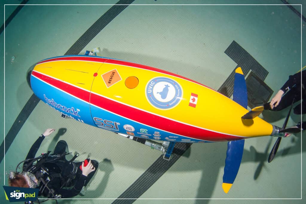 Electric surfboard with colorful design and safety logos on a testing platform.