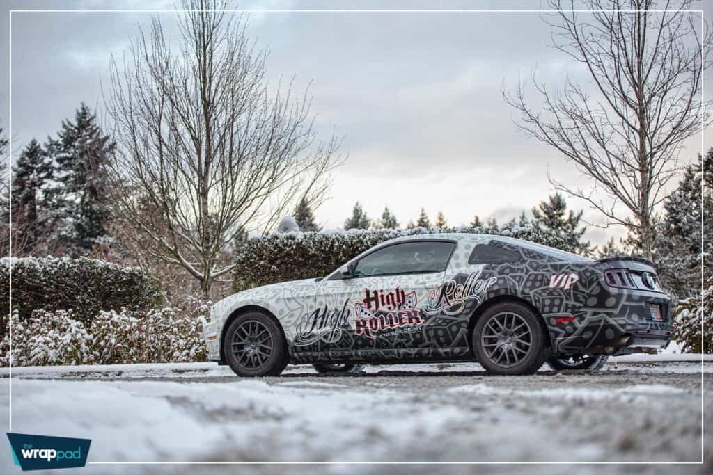 Custom vehicle wrap on a black car with intricate graphics in snowy landscape.