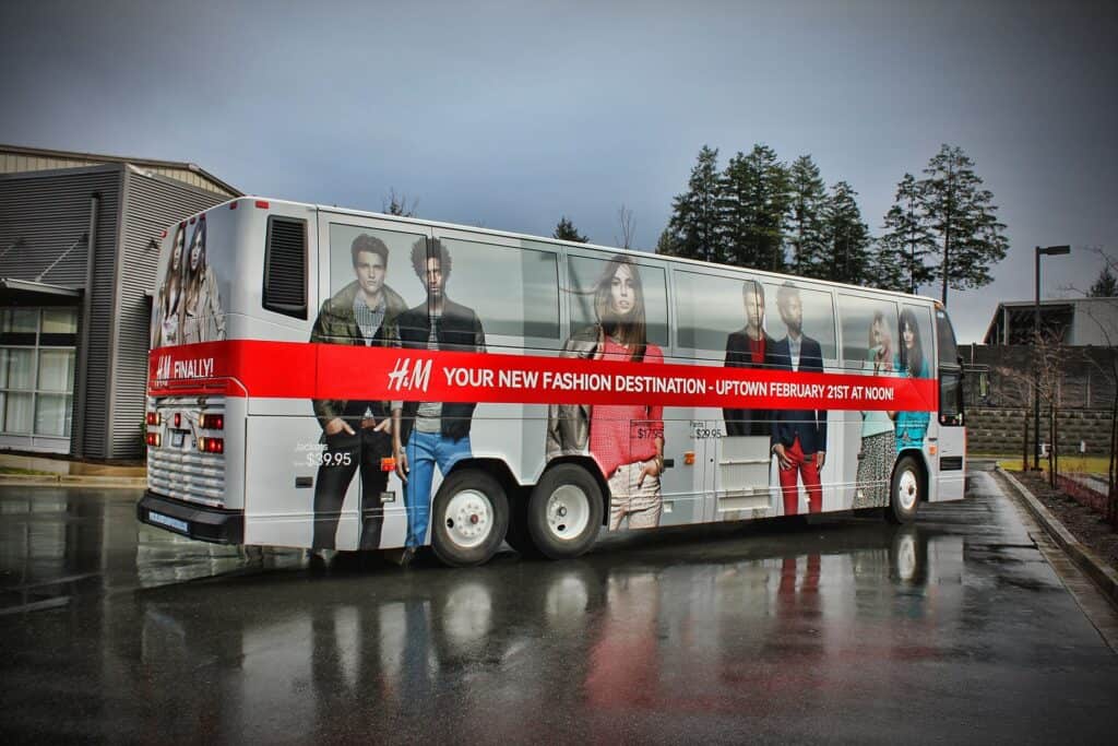 Fashion bus wrap featuring models and a bold red promotional banner.