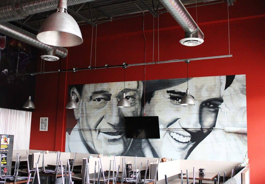 Mural of a smiling man and woman on a restaurant wall, creating a lively atmosphere.