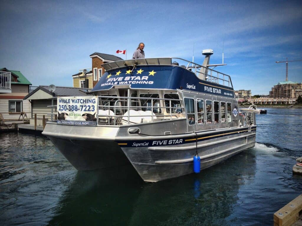 Boat with "FIVE STAR" whale watching boat docked near waterfront buildings.