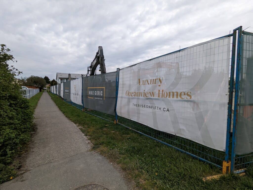 Construction site fence with luxury oceanview homes advertising banner in Victoria.