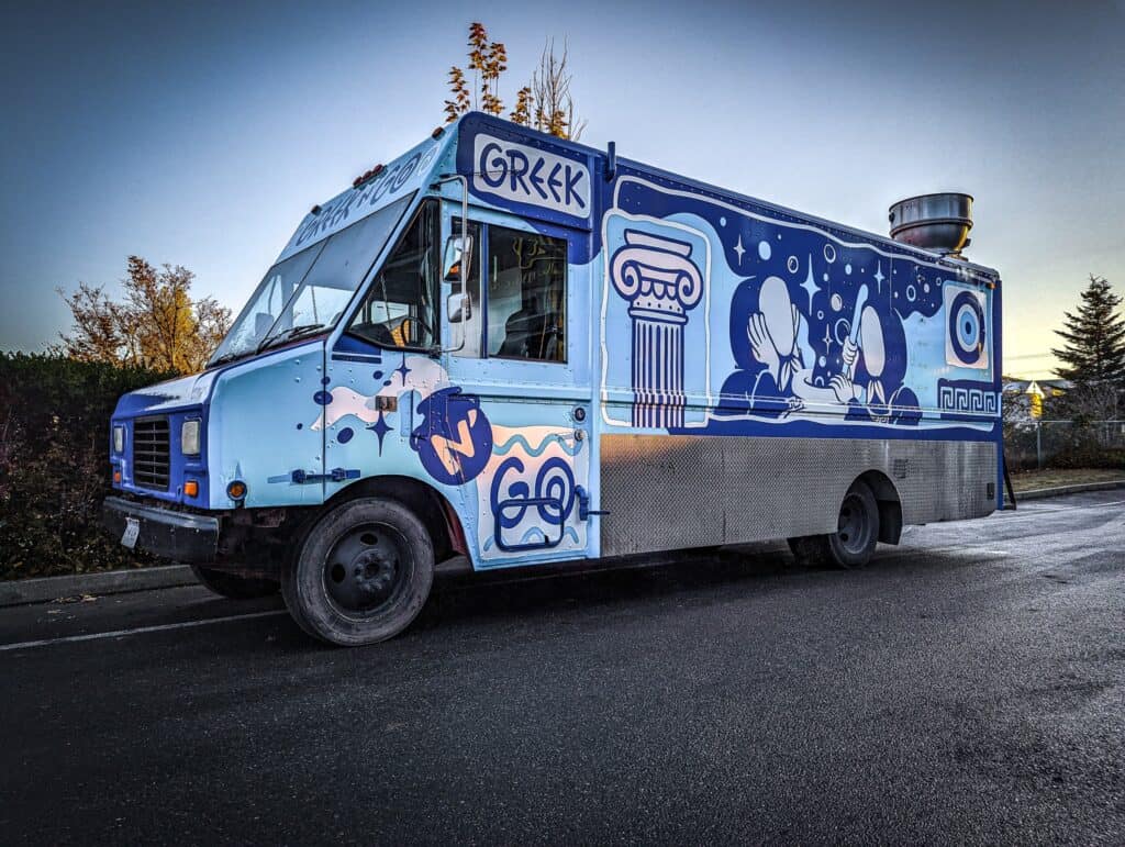 Greek food truck with vibrant blue and white Greek-themed graphics.