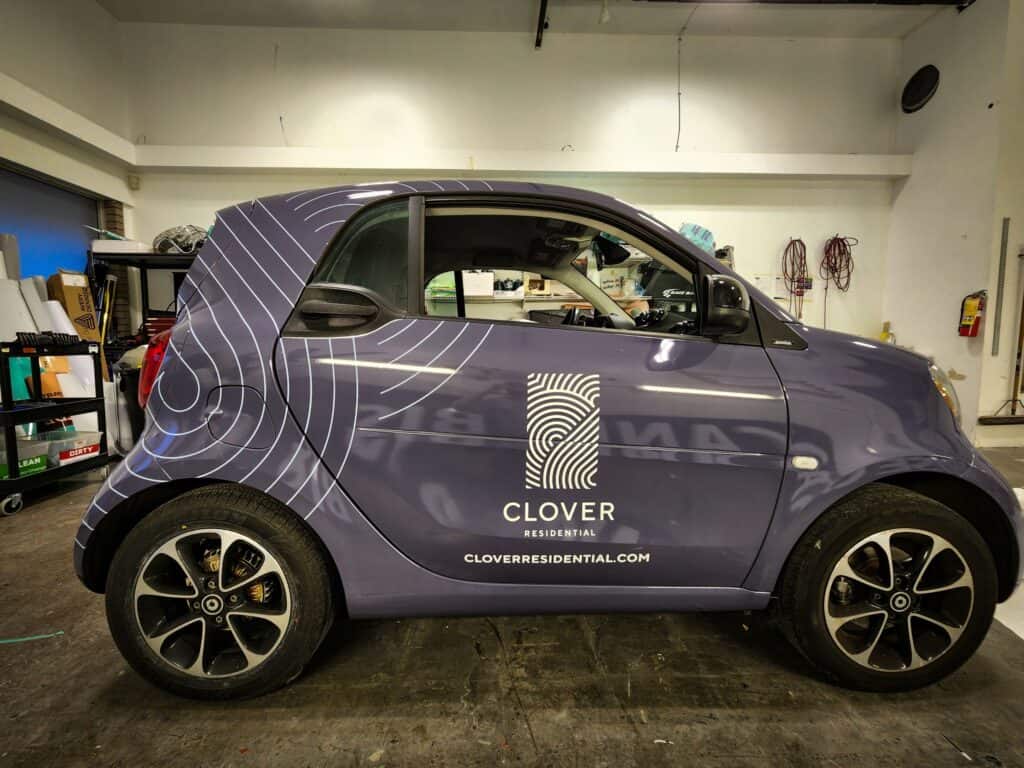 Smart car with custom Clover Residential signage on the side.