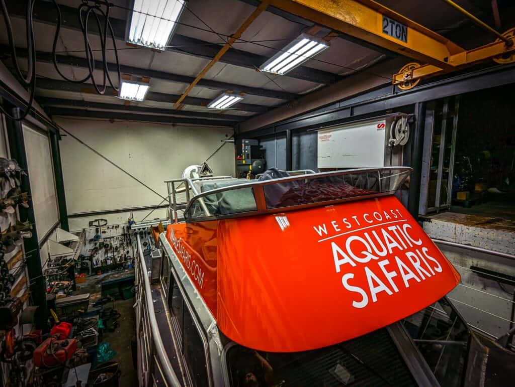 Aquatic Safaris boat sign with vibrant orange color and white logo, displayed inside a workshop.