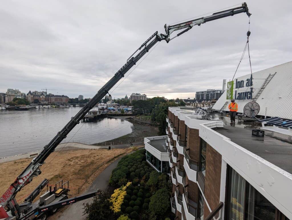 Crane lifting sign for installation on building rooftop in Victoria.