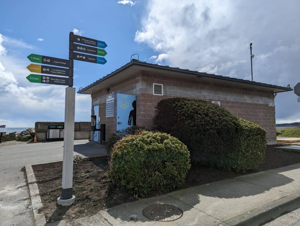 Directional signs and building at Victoria location with bushes and cloudy sky.