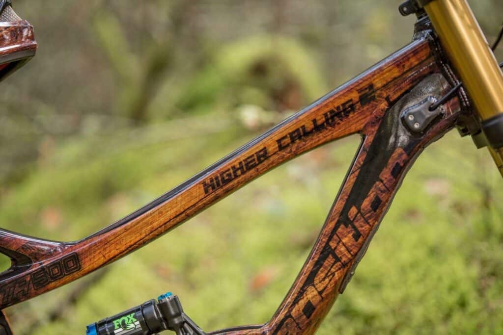 Custom mountain bike frame with wood finish and "Higher Calling" branding.