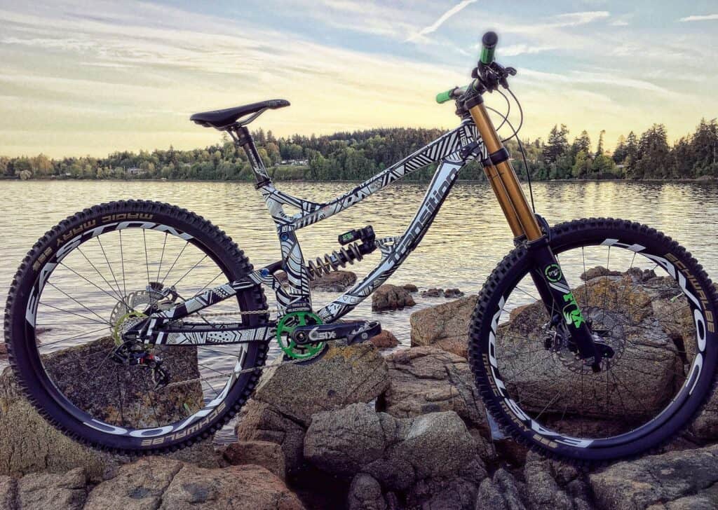 Mountain bike on rocky shoreline with water and trees in the background.