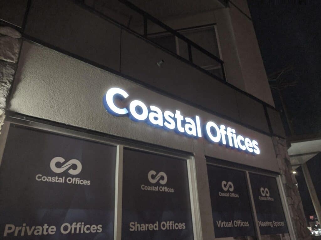 Illuminated Coastal Offices sign on building at night in Victoria.