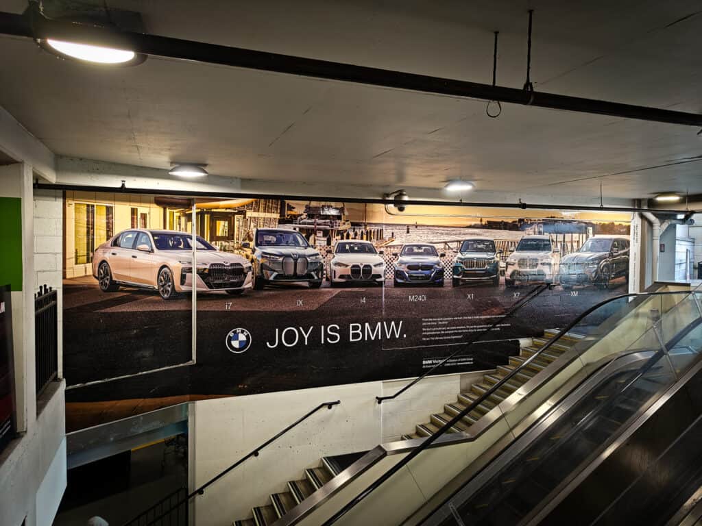 Indoor parking garage with BMW cars and a large promotional wall display.