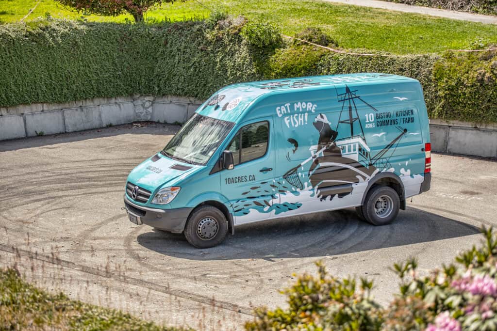 Delivery van with fish-themed advertising promoting fresh seafood and fishing supplies.