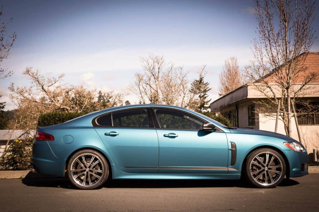 Blue luxury sedan parked on the street with trees in the background.