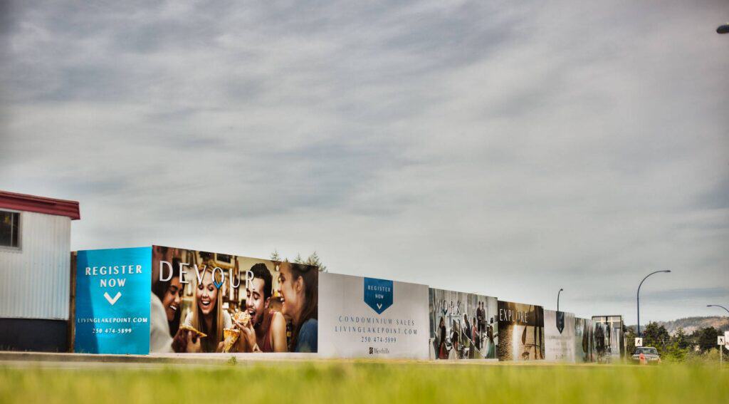 Custom signs and vehicle wraps displayed on a long outdoor wall in Victoria.