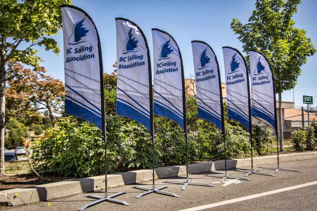 Row of BC Sailing Association feather flags displayed outdoors on a sunny day.
