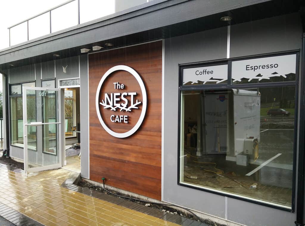 Sign for The Nest Cafe with wooden background and illuminated logo.